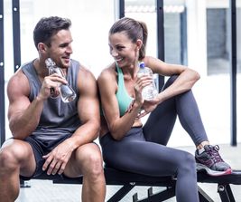 Muscular couple discussing on the bench and holding water bottle